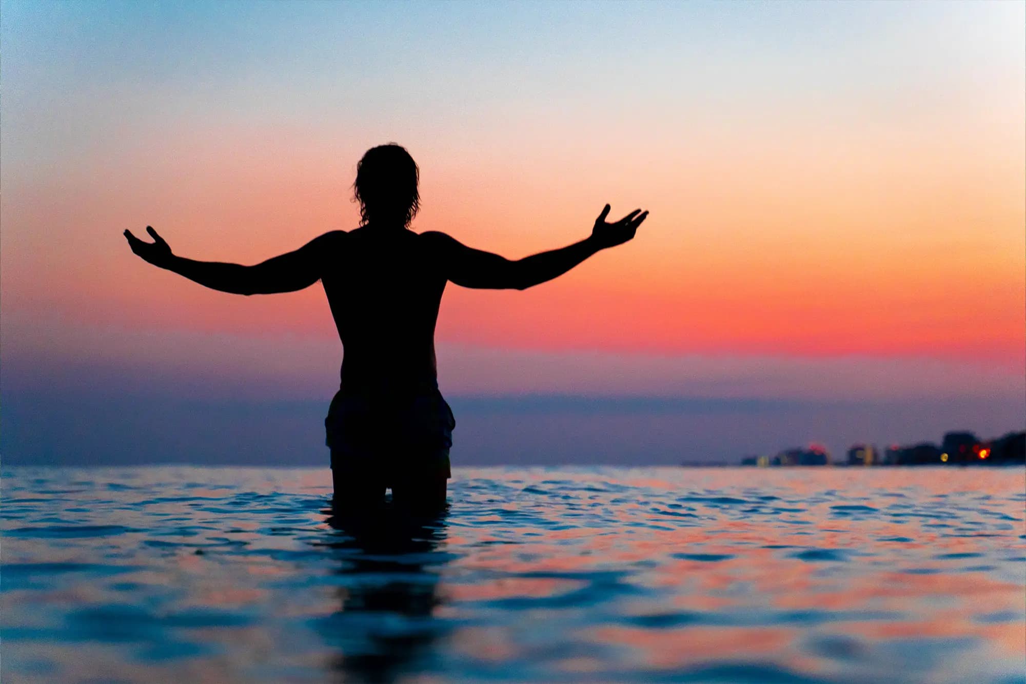 Silhouette of Cam standing in the ocean with arms open at sunset