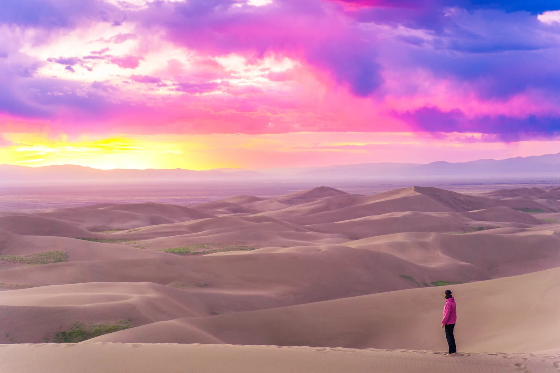 Cam on a dune crest watching a magenta and violet sunset over a sea of sand