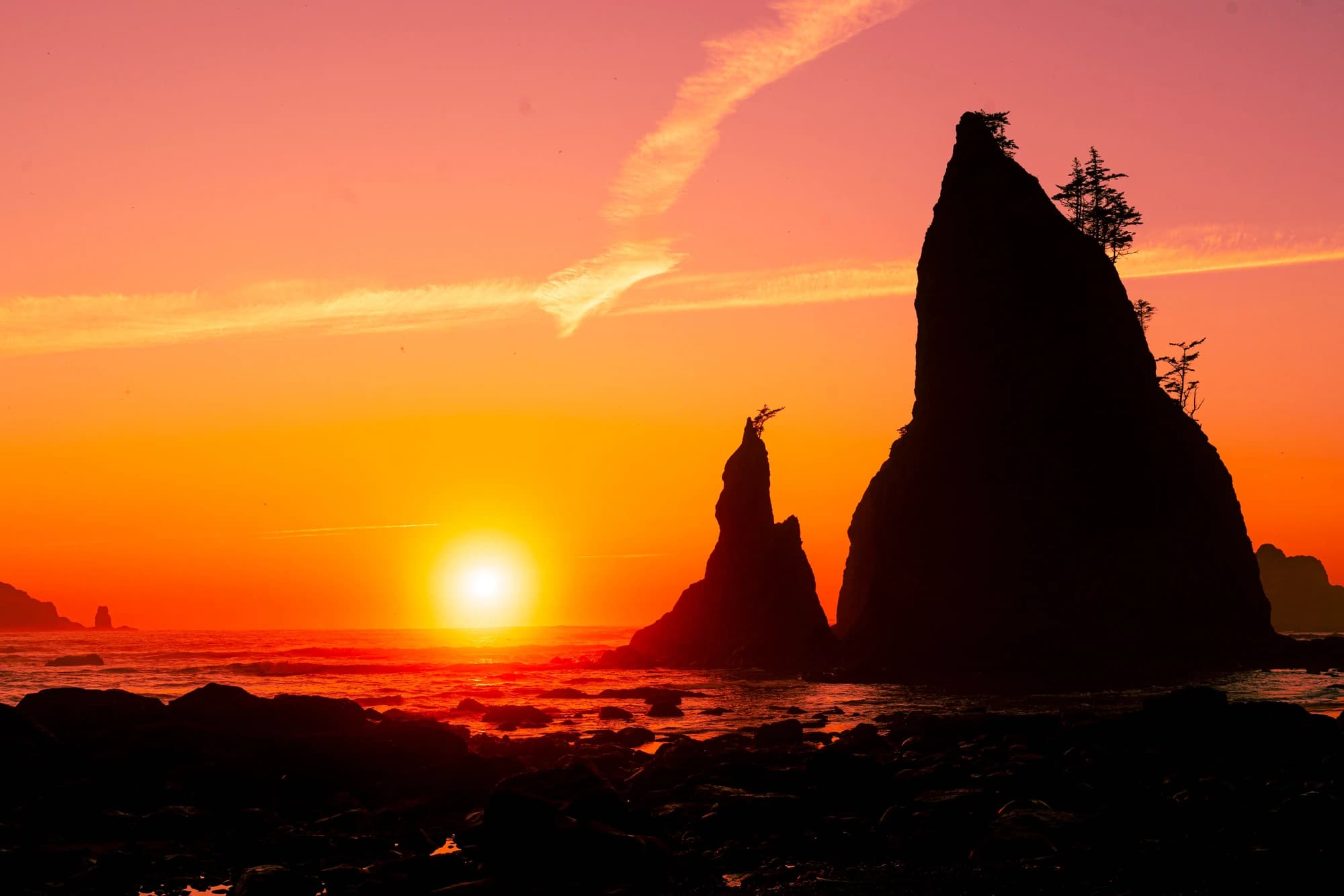 The sun setting into the ocean beside towering silhouetted sea stacks