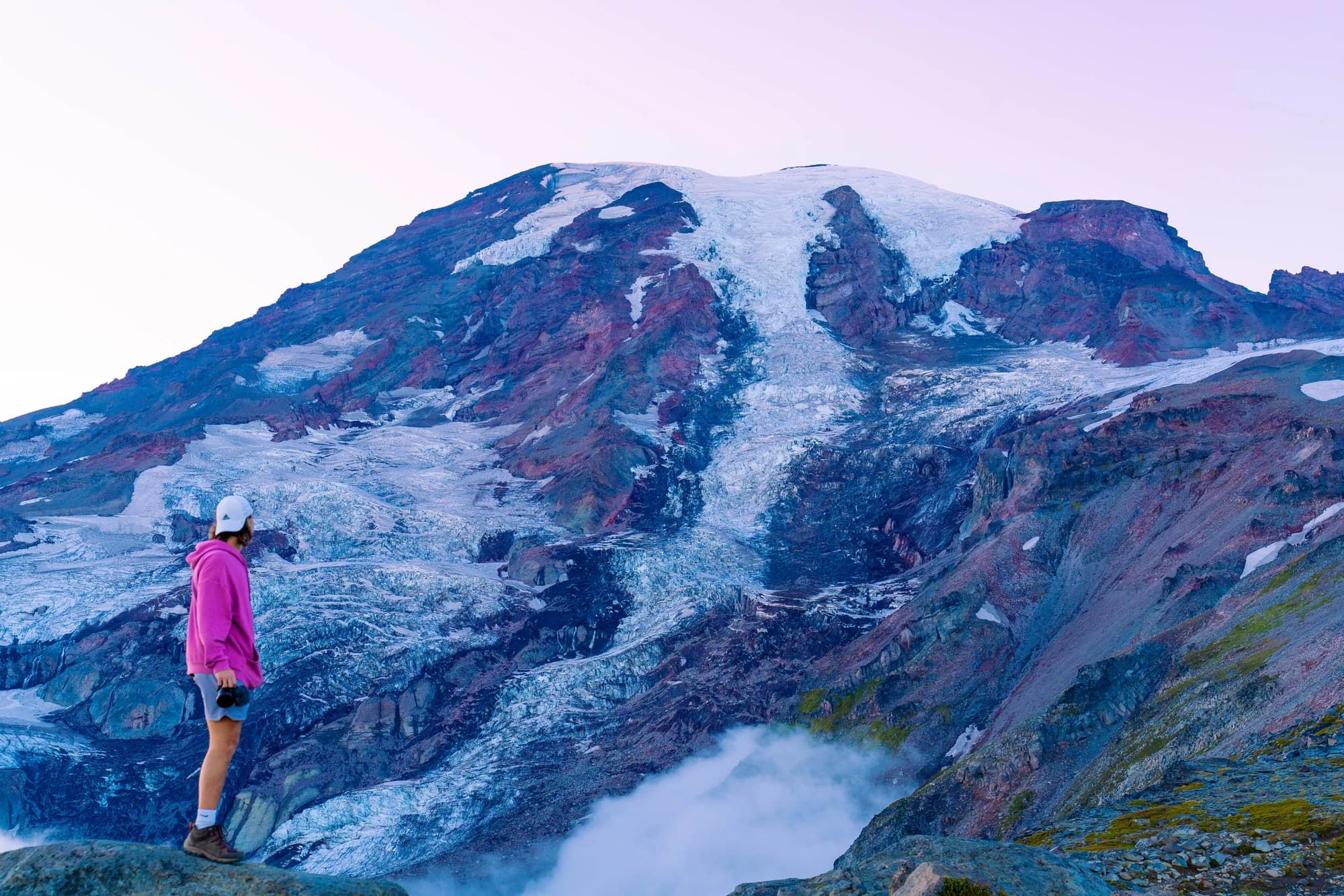 Cam in a pink hoodie facing a glacier-covered volcano at dawn