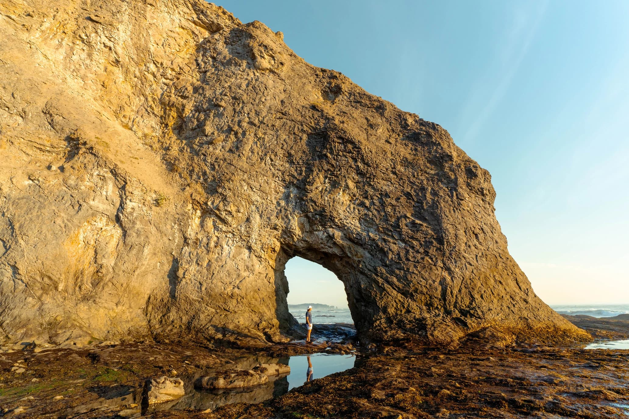 Cam standing inside a sea arch at low tide, reflected in a tide pool